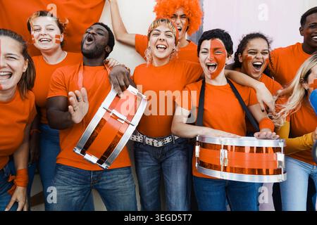 Orange sport fans having fun supporting their team - Football supporters having fun at world competition event - Main focus on center girls faces Stock Photo