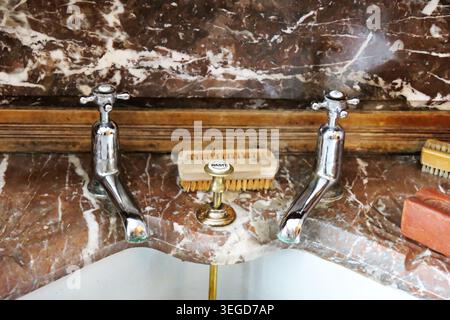 Close-up of separate vintage chrome water taps with cross head handles installed on a brown veined marble washbasin splashblack. Stock Photo