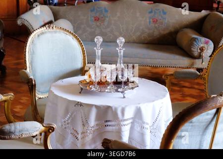 Two elegant vintage crystal decanters filled with amber liquor and fortified wine with etched cordial glasses on a silver serving tray. Stock Photo