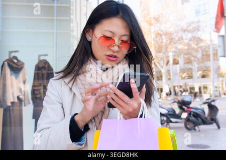 Young woman with shopping bags using smartphone on city street Stock Photo