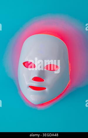 Futuristic LED face mask glowing in neon light on blue background. Minimal LED light therapy mask concept. Stock Photo