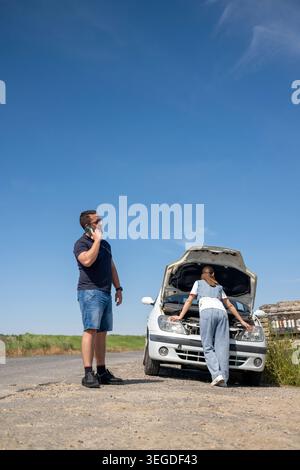 Couple calling for help with car broken down on roadside Stock Photo