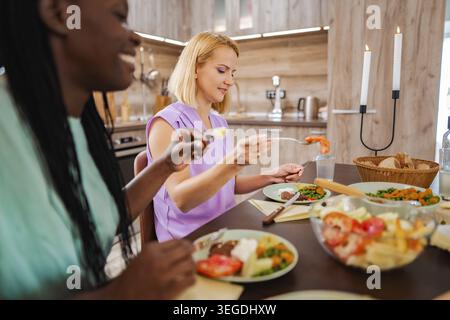 Friends enjoying a delicious homemade meal in a cozy kitchen Stock Photo