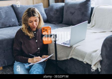 Woman freelancer taking notes during online meeting or remote training session while working from home. High quality photo Stock Photo