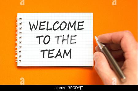 Support, help welcome to the team symbol. Concept words Welcome to the team on beautiful white note. Beautiful orange background. Businessman's hand. Stock Photo