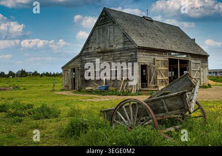 View of a rustic weathered wooden barn and an old cart in a green field under a cloudy sky in Edgartown, Massachusetts, United States. Stock Photo