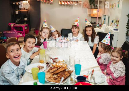 Group of children celebrating a birthday in a decorated room with cake and snacks during a daytime party Stock Photo