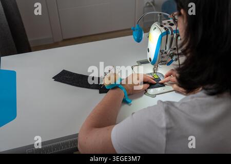 Female seamstress sewing clothes and working with textile materials in creative workshop. Back view of dressmaker during tailoring process with sewing Stock Photo