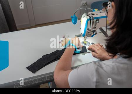 Female seamstress sewing clothes and working with textile materials in creative workshop. Back view of dressmaker during tailoring process with sewing Stock Photo