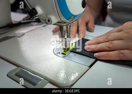 Close up view of sewing process with fabric, threads and sewing machine during clothing creation. Detailed textile work with stitches, tailoring equip Stock Photo