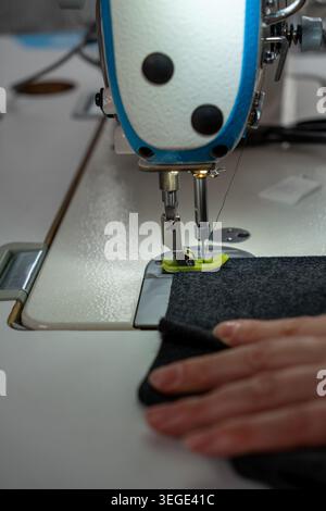 Vertical close up of sewing process with fabric, threads and sewing machine during clothing production. Detailed textile work with stitches, tailoring Stock Photo