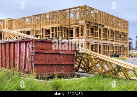 Workers build new structure using wood materials near large dumpster in city landscape Stock Photo