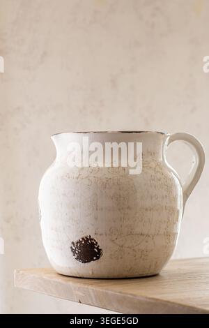 A rustic white ceramic jugs with handles and a weathered brown pattern on a wooden surface. Stock Photo