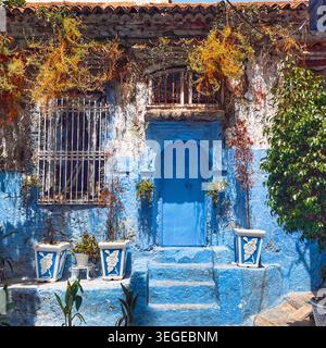 Weathered blue-painted facade with arched doorway, barred windows, and decorative planters in the medina of Chefchaouen, Morocco. 3rd August 2025. Stock Photo