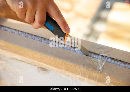 Hand opening cardboard package with utility knife outdoors. Concept: unboxing process Stock Photo
