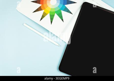 Top view of digital tablet with stylus pen beside color wheel chart on light blue surface, graphic design and digital art tools. Stock Photo