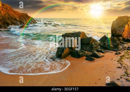 sunset over huge stones on the sandy beach. wonderful holiday season background at the sea. clouds on the blue sky above horizon. view of waves washin Stock Photo