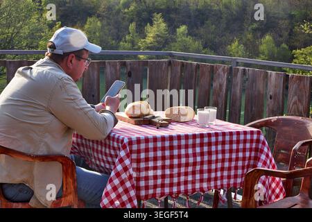 Man Using Smartphone During Rustic Countryside Breakfast Stock Photo