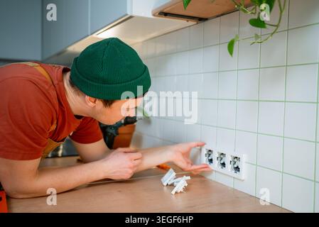 Young man electrician installing multiple new electrical sockets and power outlets in a modern kitchen while working on home renovation and upgrade projects Stock Photo