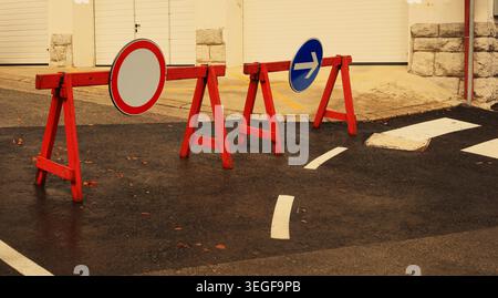 Temporary road closed signs and red-and-white warning barriers blocking an asphalt street during roadworks. Stock Photo