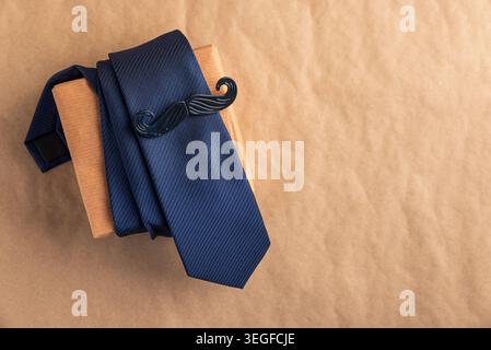 Blue necktie and stylish mustache tag on a brown kraft-wrapped gift box, top-view flat lay suggesting a thoughtful Father's Day or men's occasion gift Stock Photo