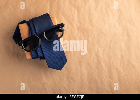 Blue necktie and stylish glasses on a brown kraft-wrapped gift box, top-view flat lay suggesting a thoughtful Father's Day or men's occasion gift with Stock Photo