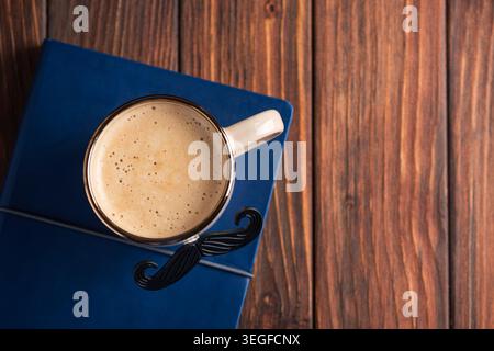 Mustache mug filled with hot coffee sitting on a blue notebook, creating a thoughtful gift concept for Father's Day or male celebrations, presented on Stock Photo