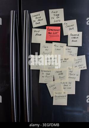 Notes are stuck on a refrigerator in a kitchen. Each note contains reminders for different tasks, like visiting family, fixing things, and appointments. The notes help keep track of daily jobs. Stock Photo