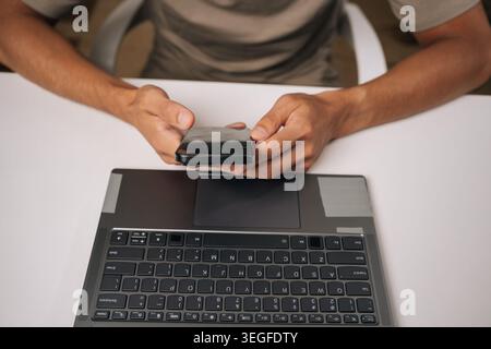 Top view of unrecognizable freelancer male working late at night in home office, using smartphone and laptop to manage business tasks and meet Stock Photo