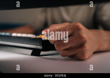 Male hands typing on mechanical keyboard with colorful keycaps in dark office, suggesting focused work or late-night coding session, close-up. Stock Photo
