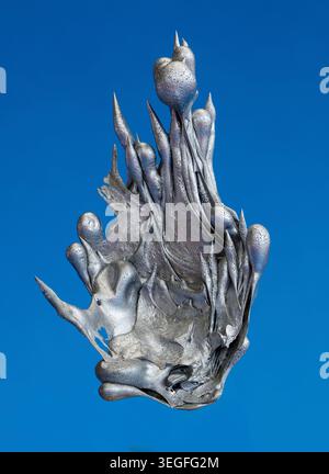 Solidified molten aluminium alloy forms an eerie alien-like sculpture against a vivid blue background with dramatic copy space. Stock Photo