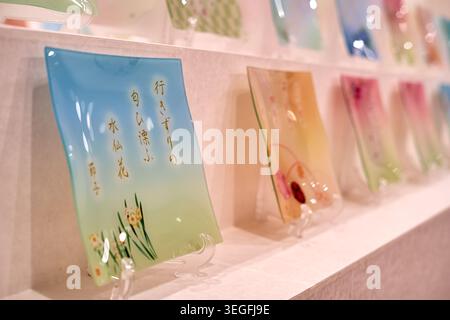 A close-up view of decorative glass plates displayed on white shelves in what appears to be a retail shop or gallery setting. The foreground features Stock Photo