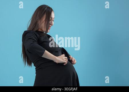 Pregnant young asian woman feeling pain holding her belly studio Stock Photo