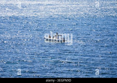 Small, white Rigid Inflatable Boat (RIB) or motorboat carrying people across a vast, sparkling blue body of water Stock Photo
