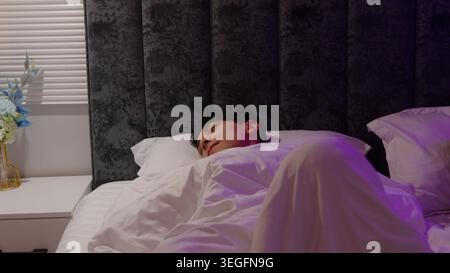 Sleeping young man lying in bed under blanket night bedroom Stock Photo