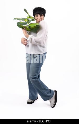 Smiling young woman carrying green plant pot walking in studio Stock Photo
