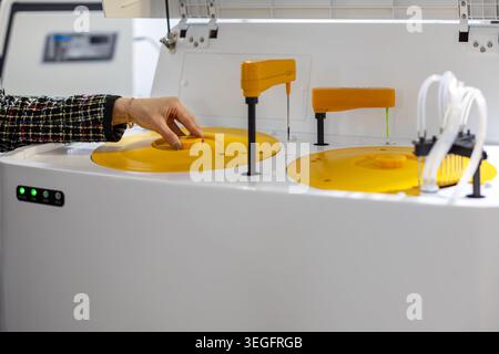 Hand operating automated laboratory analysis machine. Close up of a hand adjusting an automated laboratory analyzer with yellow trays, probes, tubing Stock Photo