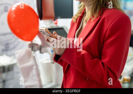 Woman in red blazer using smartphone. Close up of a woman in a red blazer using a smartphone at a bright business event with balloons. Stock Photo