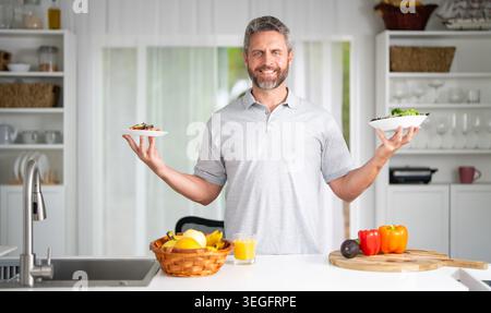 Healthy nutrition mature man. Caucasian man with healthy products at kitchen. Handsome Senior Man Eating Tasty Meal In Kitchen At Home. Elderly Man at Stock Photo