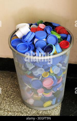 Metal mesh bin overflowing with used plastic bottle caps of various colors, representing environmental conservation, waste management, and sustainable Stock Photo