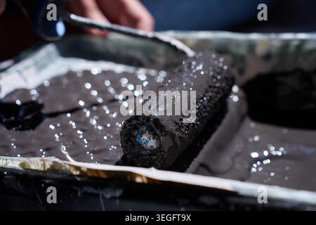 Close up of paint roller resting in tray with dark paint and hand in background. Concept of renovation and paint preparation Stock Photo