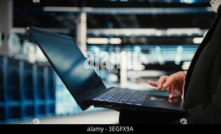 Close up of data center technician using AI LLM assistant on laptop to troubleshoot issues. Server hub specialist using artificial intelligence model on notebook to analyze system logs Stock Photo