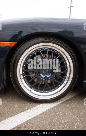 Sleek Car Wheel. Urban Scene Featuring Glossy Black Alloy Rim With Lowprofile Tire Parked On Asphalt Stock Photo