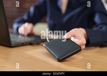 Woman connecting external hard drive to laptop at wooden desk, closeup Stock Photo