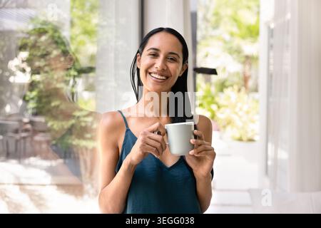 Smiling woman drinking coffee near window at home Stock Photo