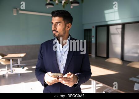 Adult businessman standing in corporate office using smartphone Stock Photo