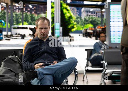 Passenger man seated waiting in crowded metropolitan bus station, showcasing daily commute and life in motion. Commuter using public transportation for everyday travel, urban transit. Stock Photo