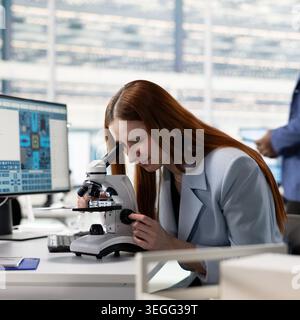 Examining microchip circuitry, microscope and woman analyzing hardware components. Evaluating electronic prototypes, optical instrument and female engineer in semiconductor factory RD office Stock Photo