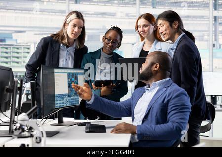 Multiethnic team of technicians monitoring microchip production in industrial plant research facility. Teamworking colleagues using devices to optimize semiconductors functionality in PCB factory Stock Photo