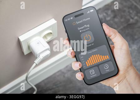 Female hand holding smartphone with smart home application interface showing energy monitoring statistics and smart plug control with a smart socket o Stock Photo